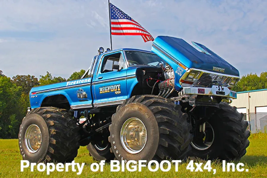 The original Bigfoot monster truck, a blue Ford pickup on massive tires with an American flag flying from the bed
